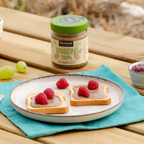 due fette biscottate con crema spalmabile di mandorle sgusciate, fluida e di colore beige, con sopra dei lamponi rossi